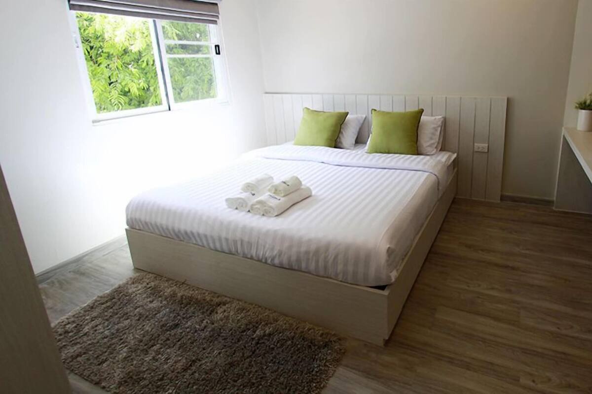 Un letto rifatto con cuscini, una piccola pianta sul comodino e un pavimento in legno.