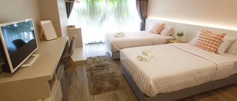 Une chambre d’hôtel avec deux lits, un bureau avec un ordinateur, une chaise, un petit tapis et une fenêtre avec des rideaux.