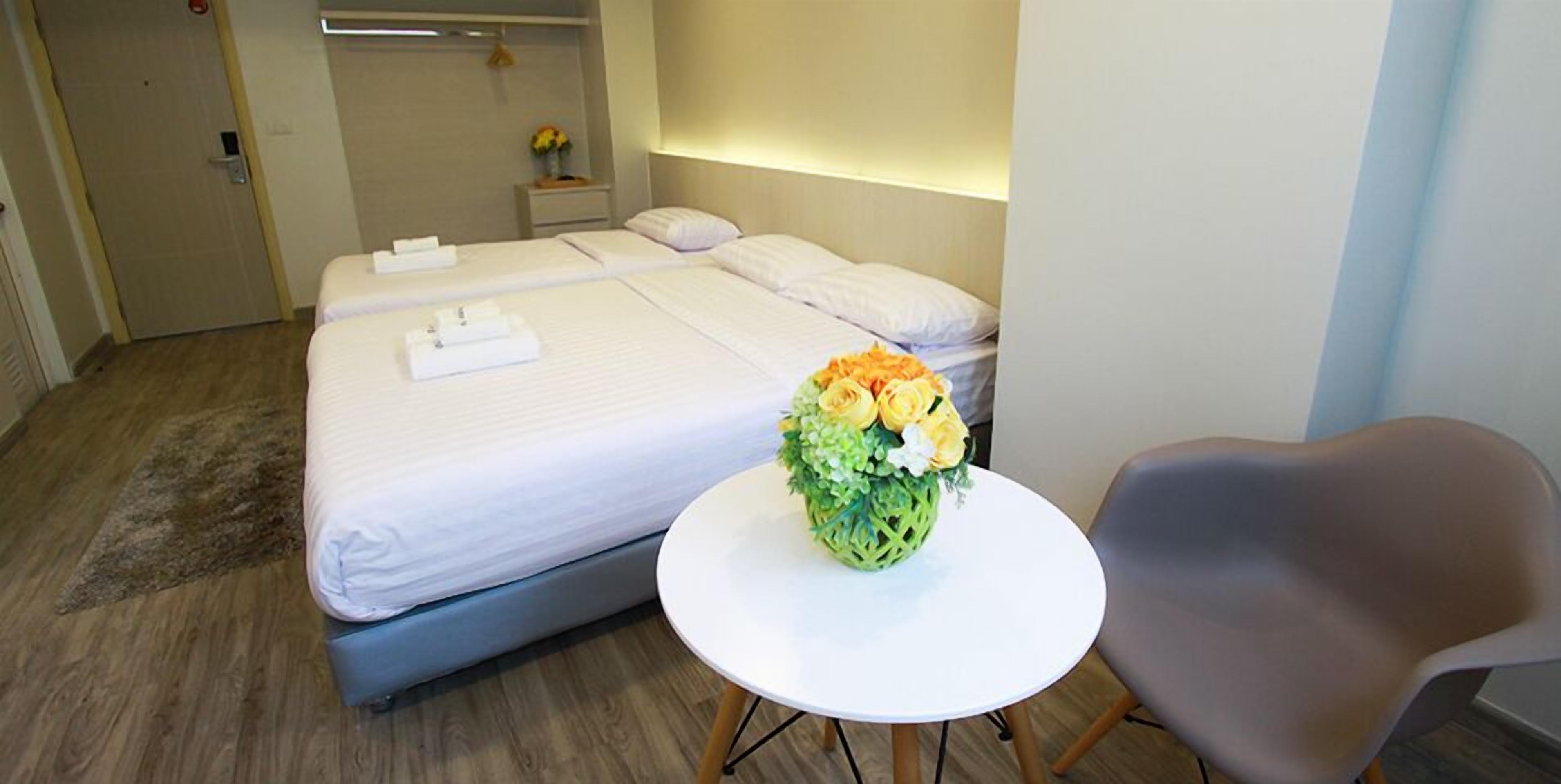 A hotel room with a double bed, a small round table with a vase of flowers, and a gray chair.