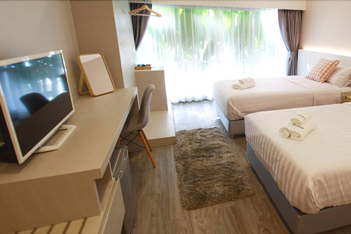 Una camera d'albergo con due letti, una scrivania con computer, una televisione e una finestra con tende.