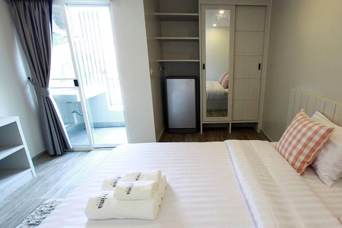 Una camera d'albergo con un letto, un armadio, un piccolo frigorifero e vista sull'esterno.