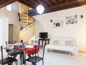 A dining area with a red tablecloth, black chairs, a spiral staircase, a white sofa, and wall art.