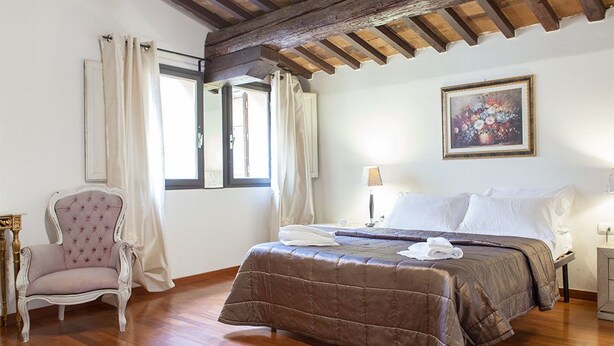 Un dormitorio con techo de madera, una cama con colcha marrón, una silla y un cuadro en la pared.