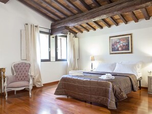 A bedroom with a wooden ceiling, a bed with a brown quilt, a chair, and a painting on the wall. - Terme Apartment (Florence)