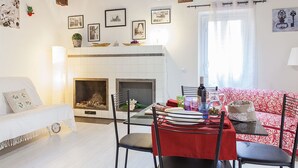 Una sala de estar acogedora con chimenea, un comedor con mantel rojo y un sofá rojo estampado.