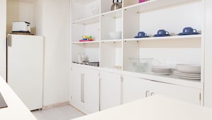 Una cocina con armarios blancos, un refrigerador y estantes con vajilla y utensilios de cocina.