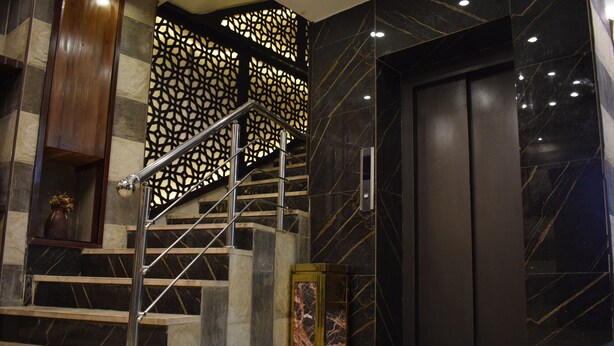 Un ascenseur moderne au design épuré, un escalier en marbre avec des rampes en métal et un panneau décoratif orné de motifs géométriques.