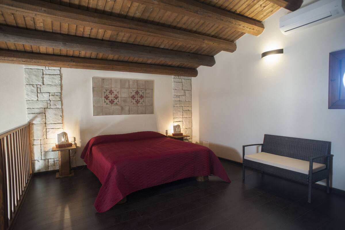 Une chambre avec un lit, un banc, un mur en pierre et un plafond en bois.