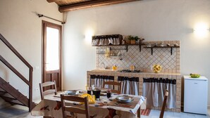Un comedor con una mesa dispuesta para cuatro, una cocina con salpicadero de azulejos y un refrigerador pequeño.