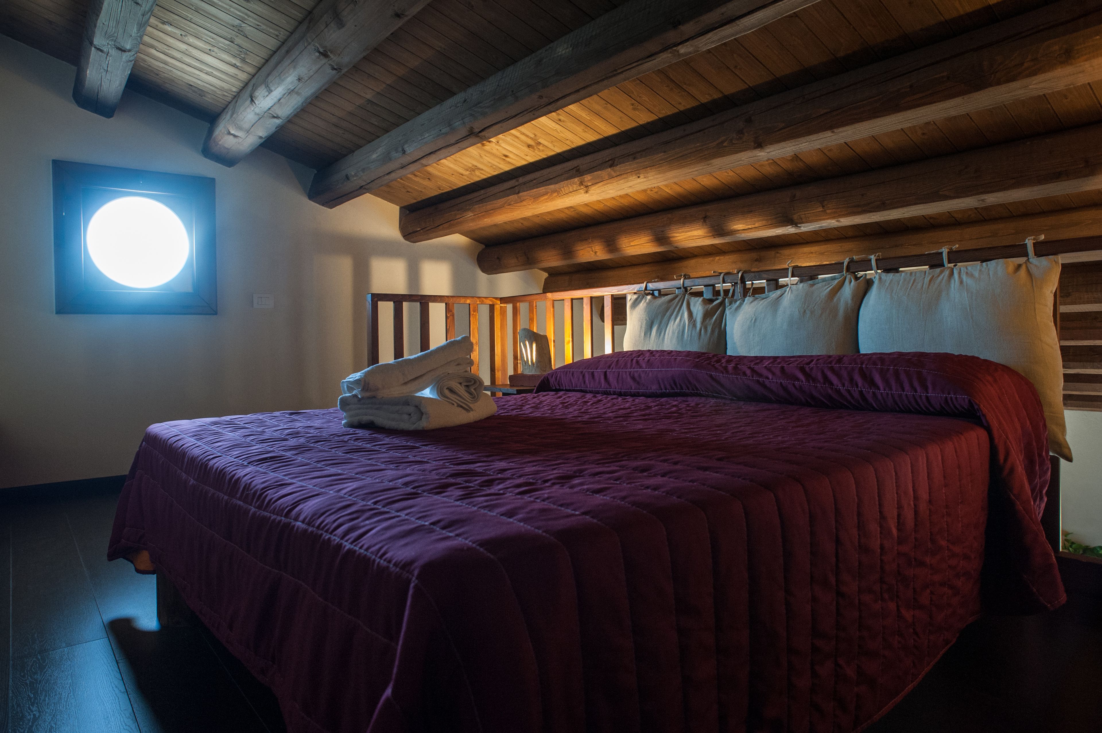 A bedroom with a large bed, wooden ceiling beams, and a skylight.