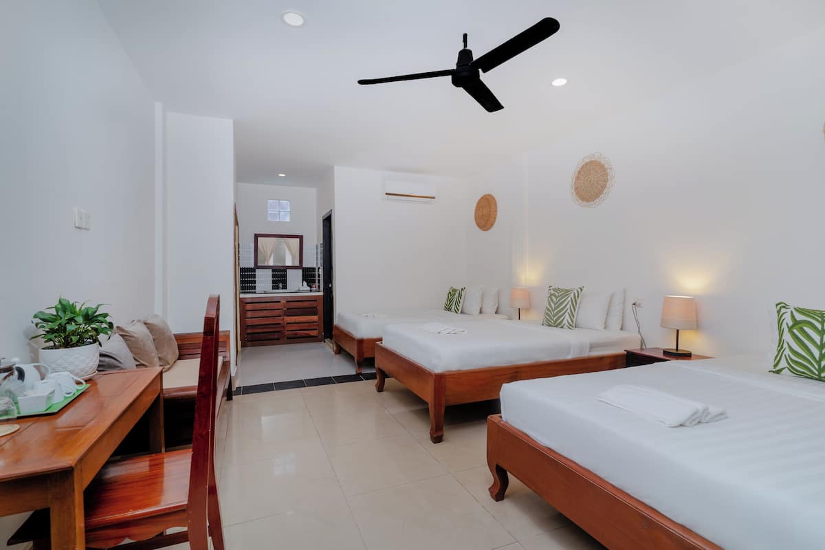 A hotel room with two single beds, a wooden desk with a chair, a dining table, and a ceiling fan.