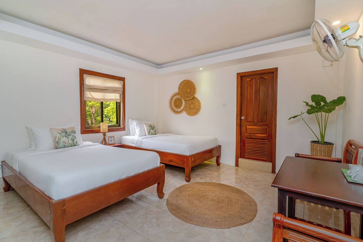 A bedroom with two beds, a dining table, a fan, and a potted plant.