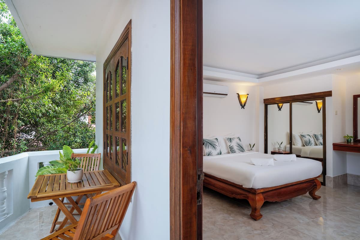 A bedroom with a wooden bed, white walls, and a balcony with a table and chairs.