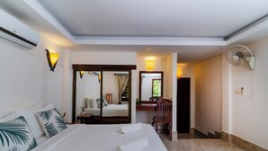 A hotel room with a large bed, a sitting area with a chair and table, a mirror, and a fan. -  River Retreat Boutique Hotel (Siem Reap)
