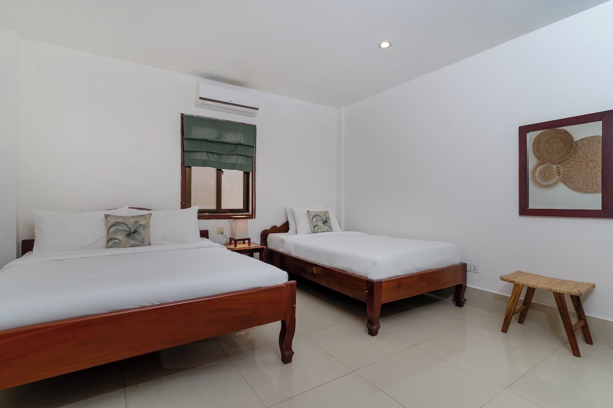A room with two wooden beds, a small wooden stool, a wall-mounted air conditioner, and a framed artwork on the wall.