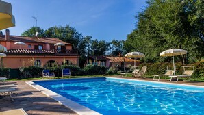 A swimming pool with lounge chairs and umbrellas, surrounded by a landscaped garden and a building with a tiled roof. - Agriturismo Bio Fattoria Casetta (Gavorrano)