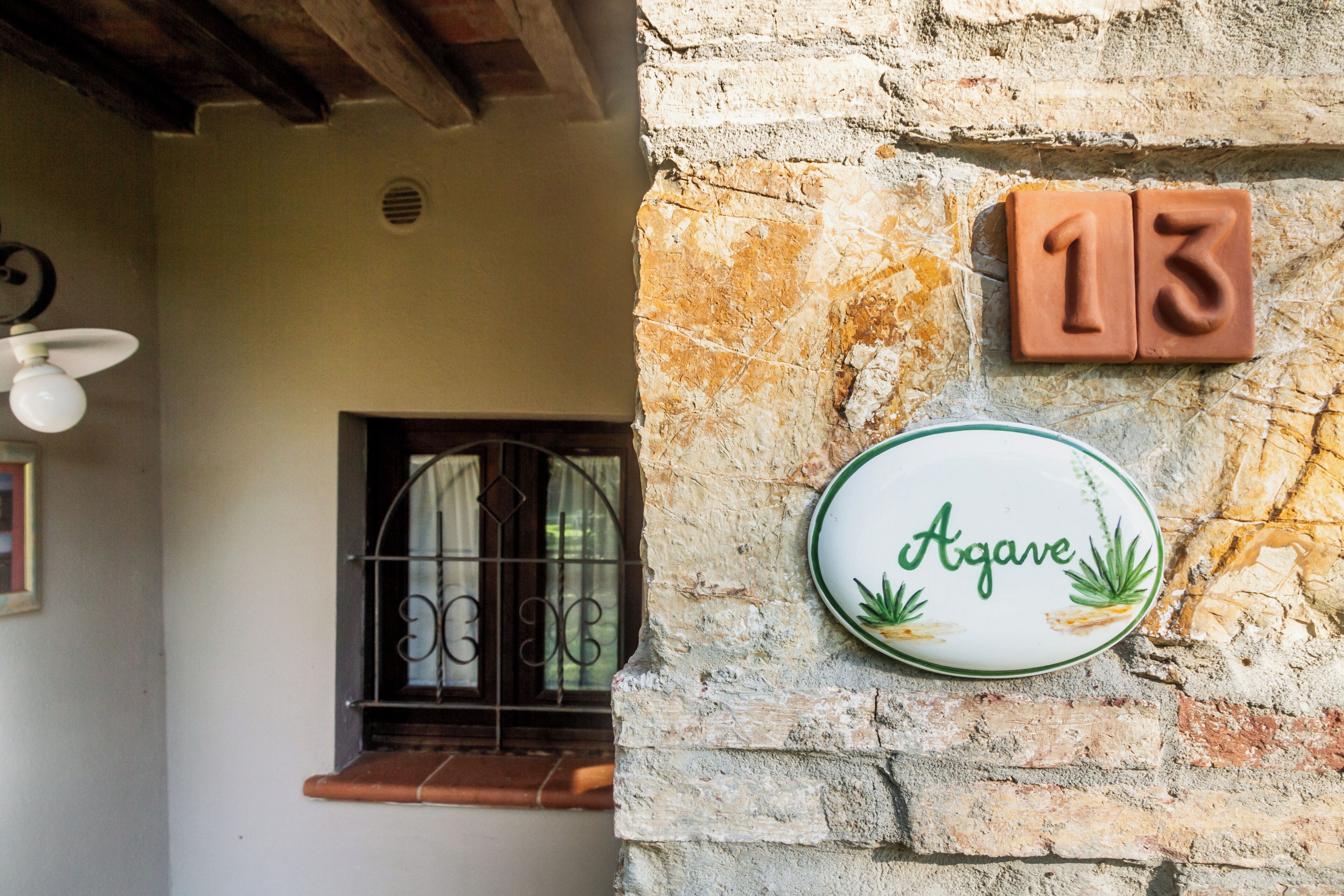 A rustic building with a stone wall, a window with metal bars, and a number plaque '13'.