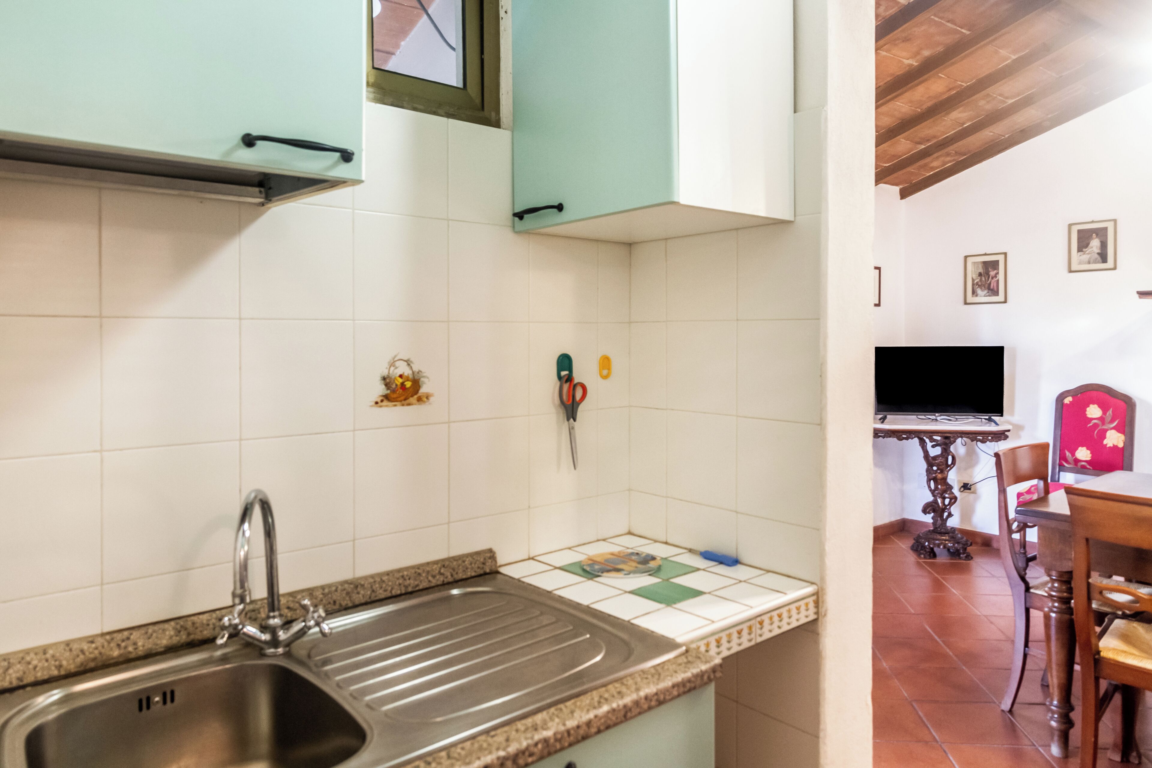 A kitchen with a stainless steel sink, a tiled backsplash, and a dining area with a table and chairs.