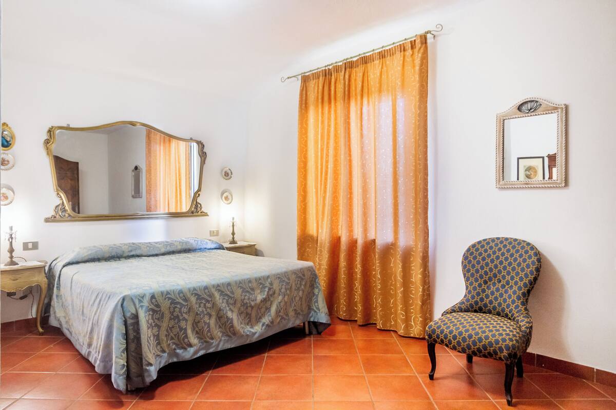 A bedroom with a bed, a chair, a mirror, and curtains.