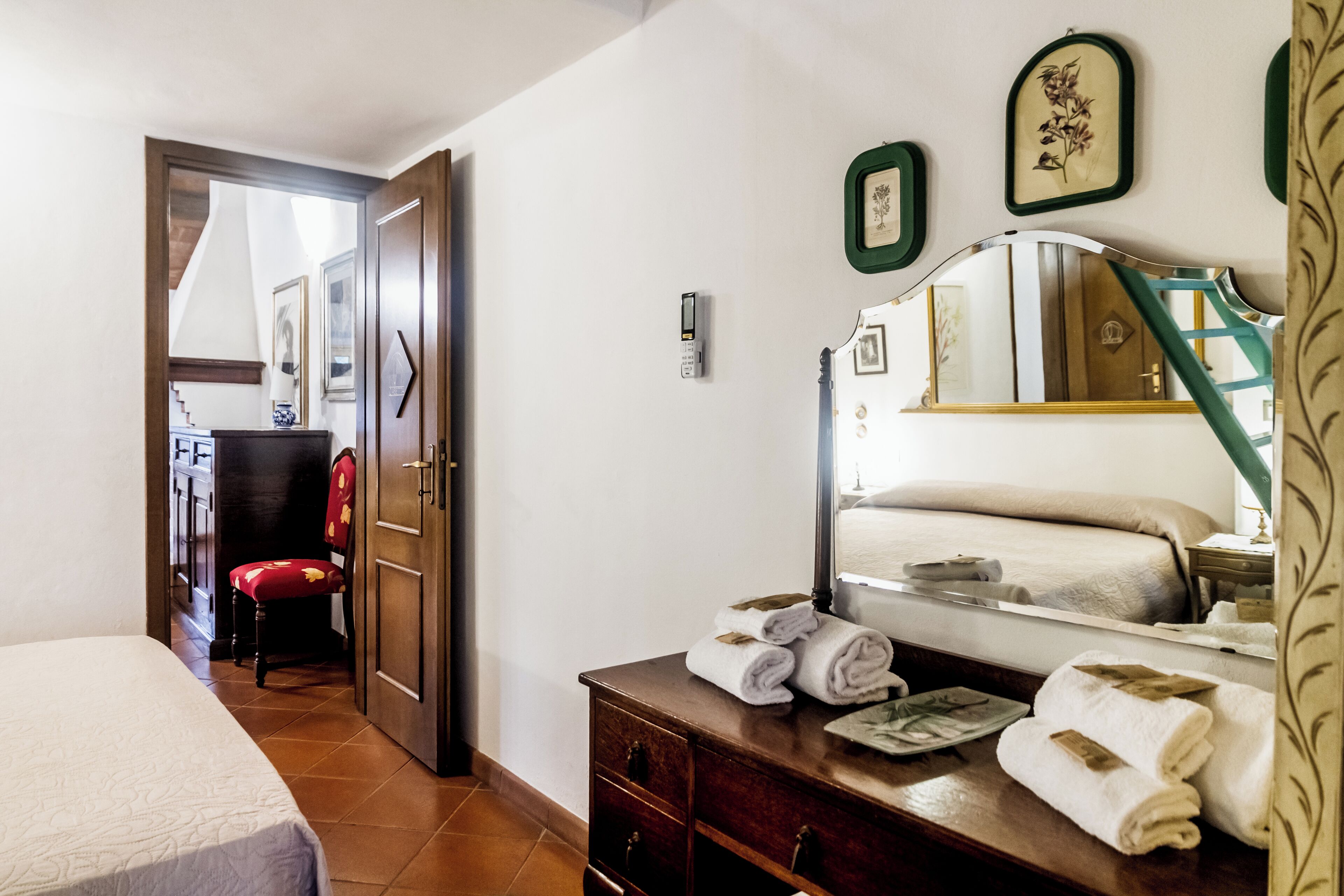 A hotel room with a bed, a wooden dresser, a mirror, and a red chair.