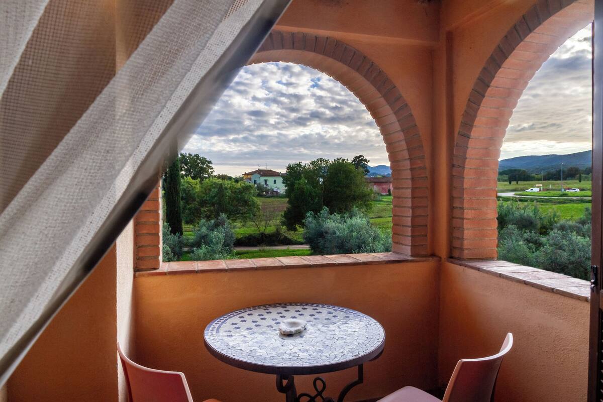 A balcony with a table and chairs, a view of greenery and a distant building.