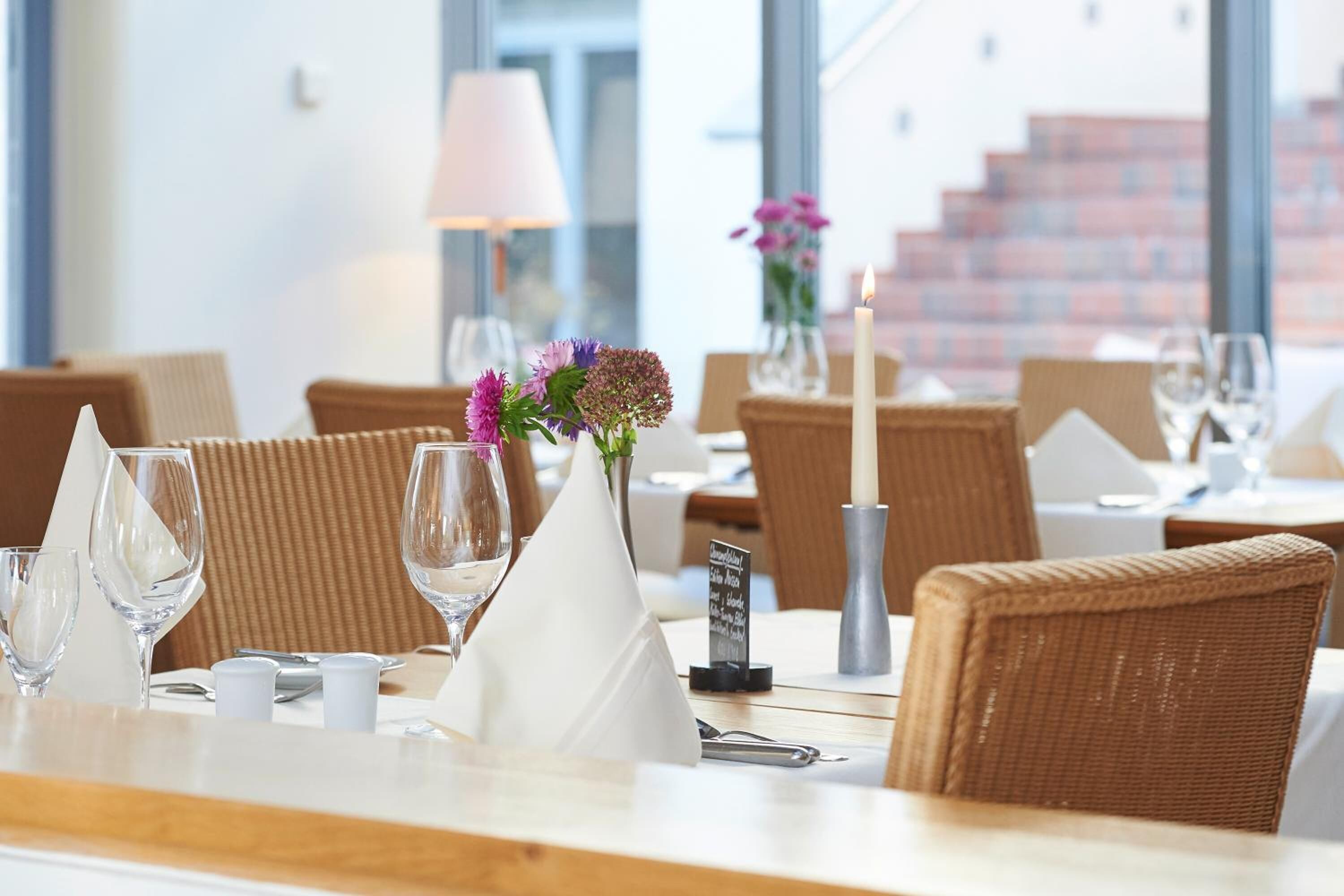 Un ambiente de restaurante con sillas de mimbre, manteles blancos y un centro de mesa con velas.