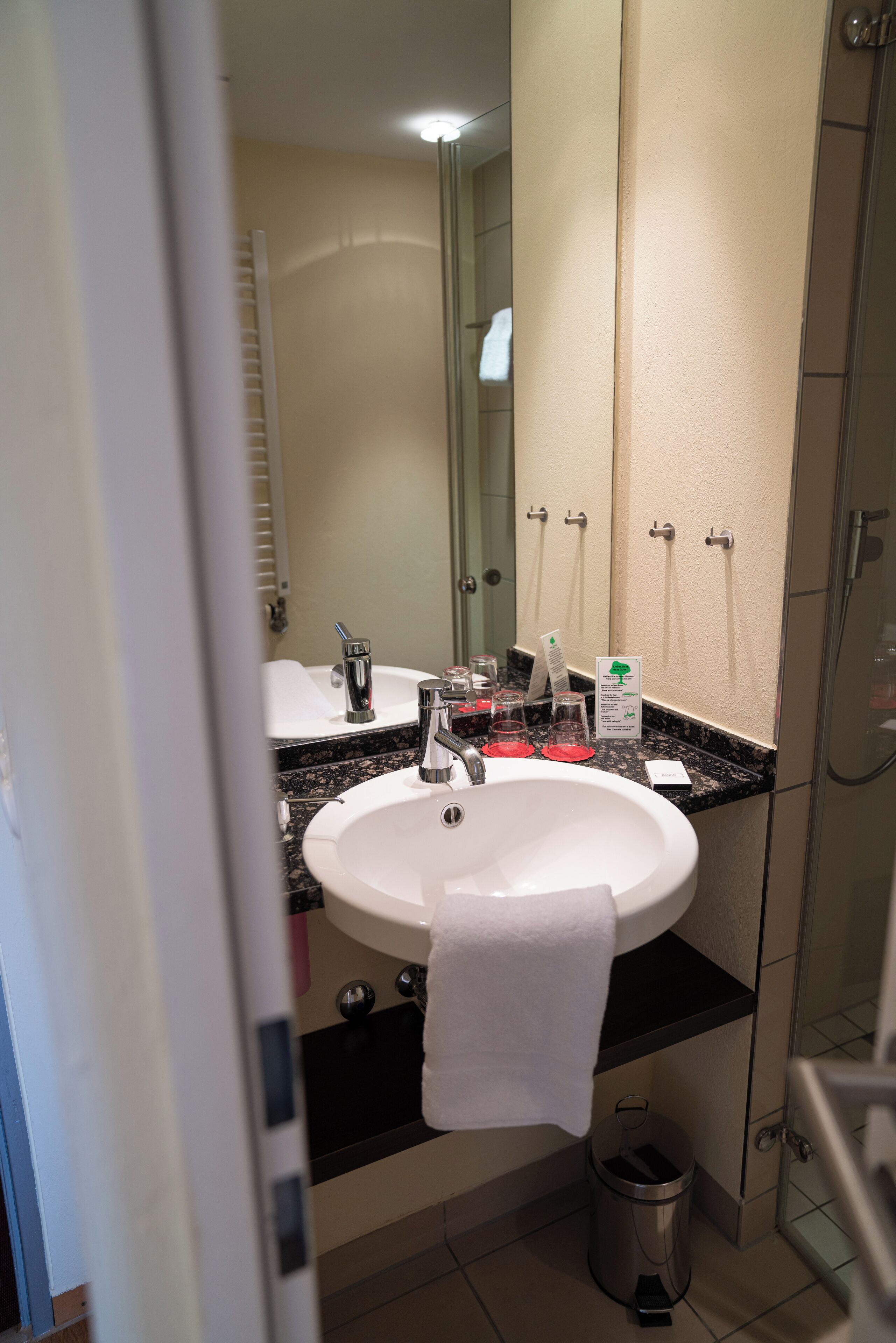 A bathroom with a white sink, a mirror, a towel hanging on the wall, and a trash can.