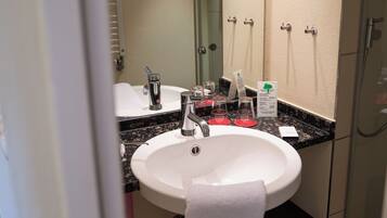 A bathroom with a white sink, a mirror, a towel hanging on the wall, and a trash can.