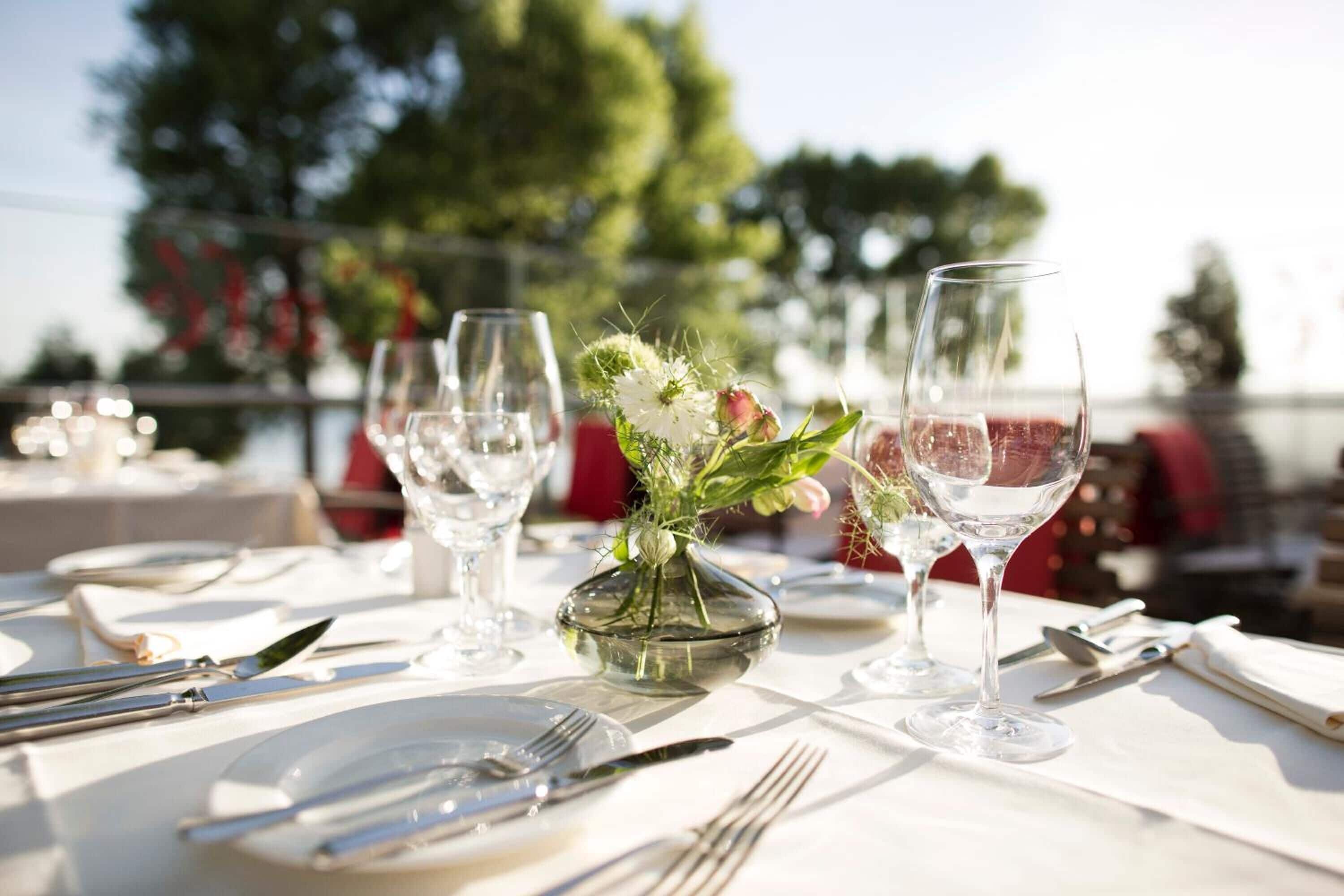 A table set for a meal with wine glasses, cutlery, and a vase with flowers.
