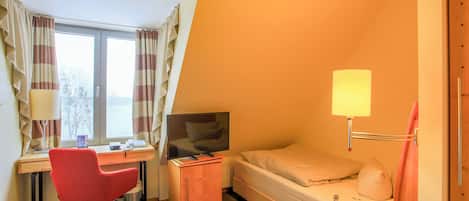 Habitación de hotel con escritorio, silla, cama, televisor y mesita de noche con lámpara.