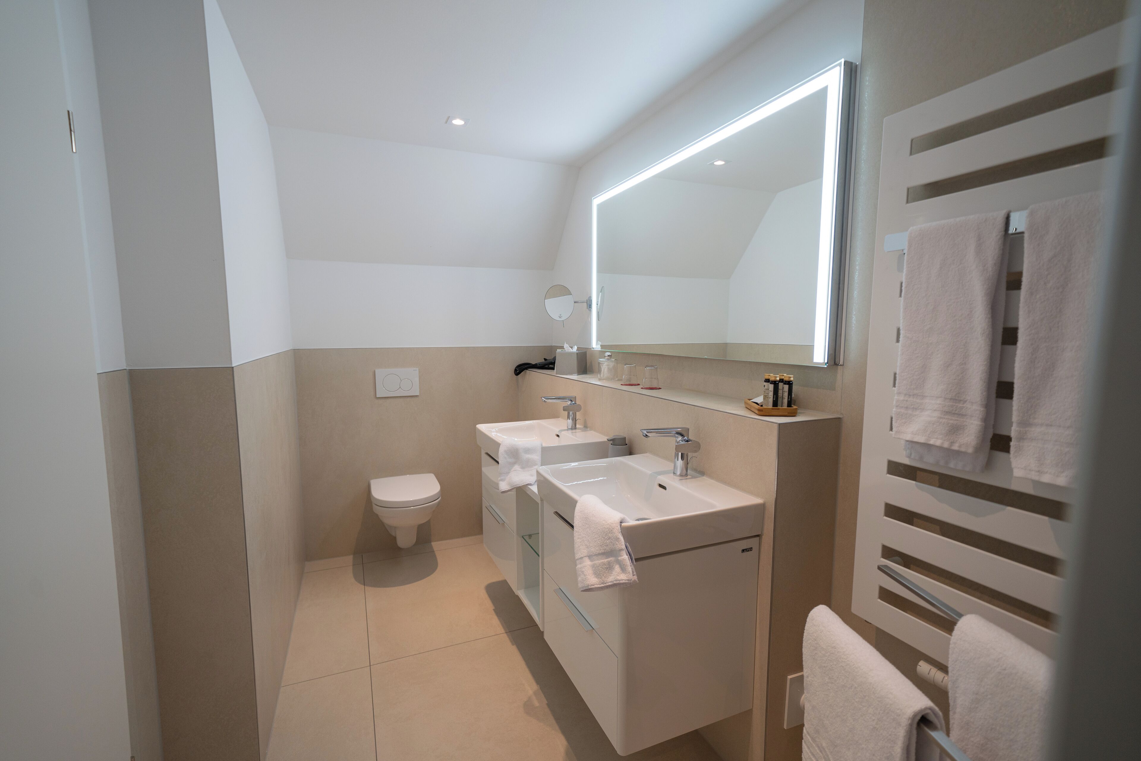 Un baño moderno con inodoro, dos lavamanos, un espejo y barras para toallas.