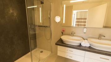 Un baño moderno con ducha de vidrio, dos lavamanos y un espejo grande.