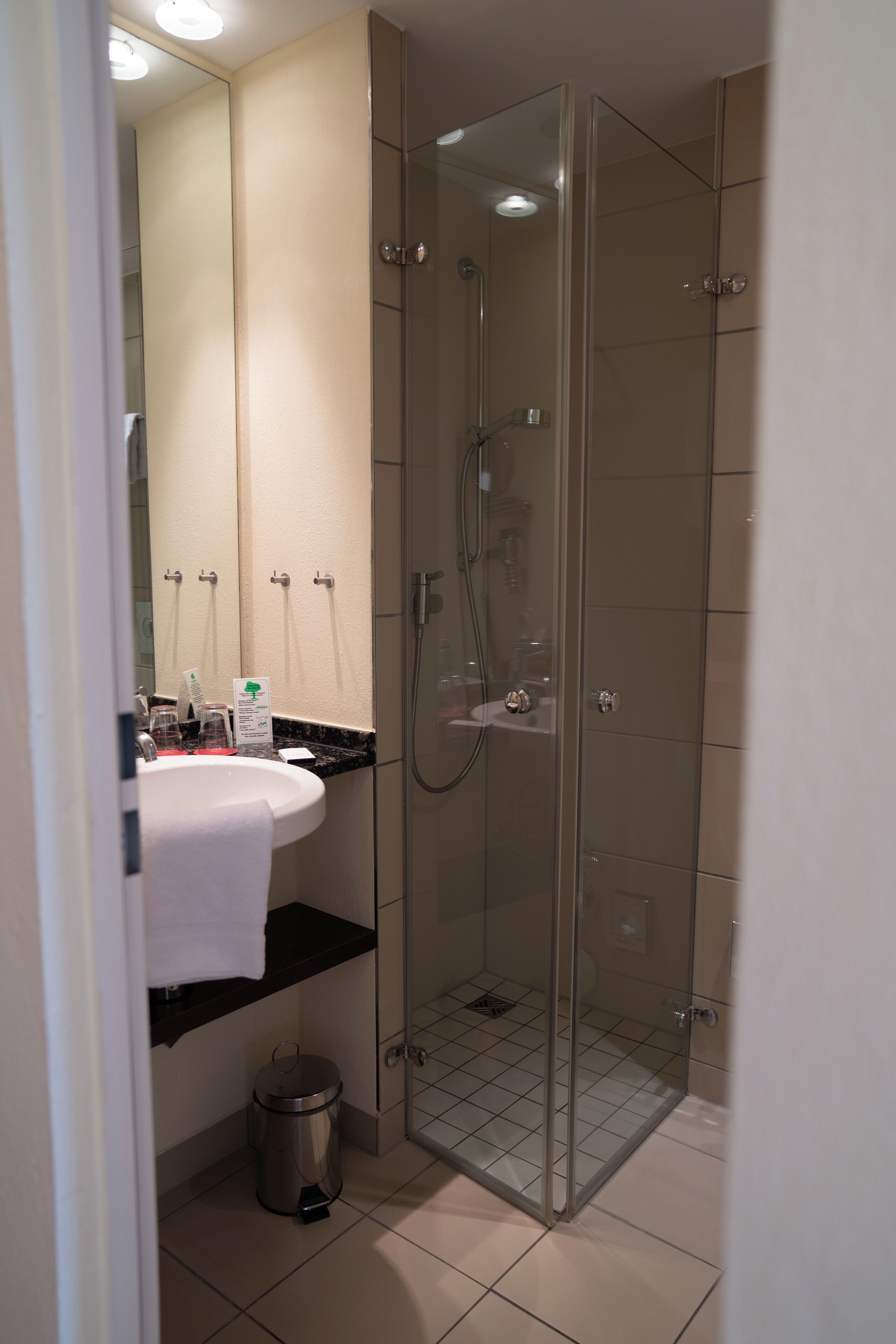 Ein modernes Badezimmer mit einer Duschkabine, einem Waschbecken mit schwarzer Ablage und einem Spiegel darüber.