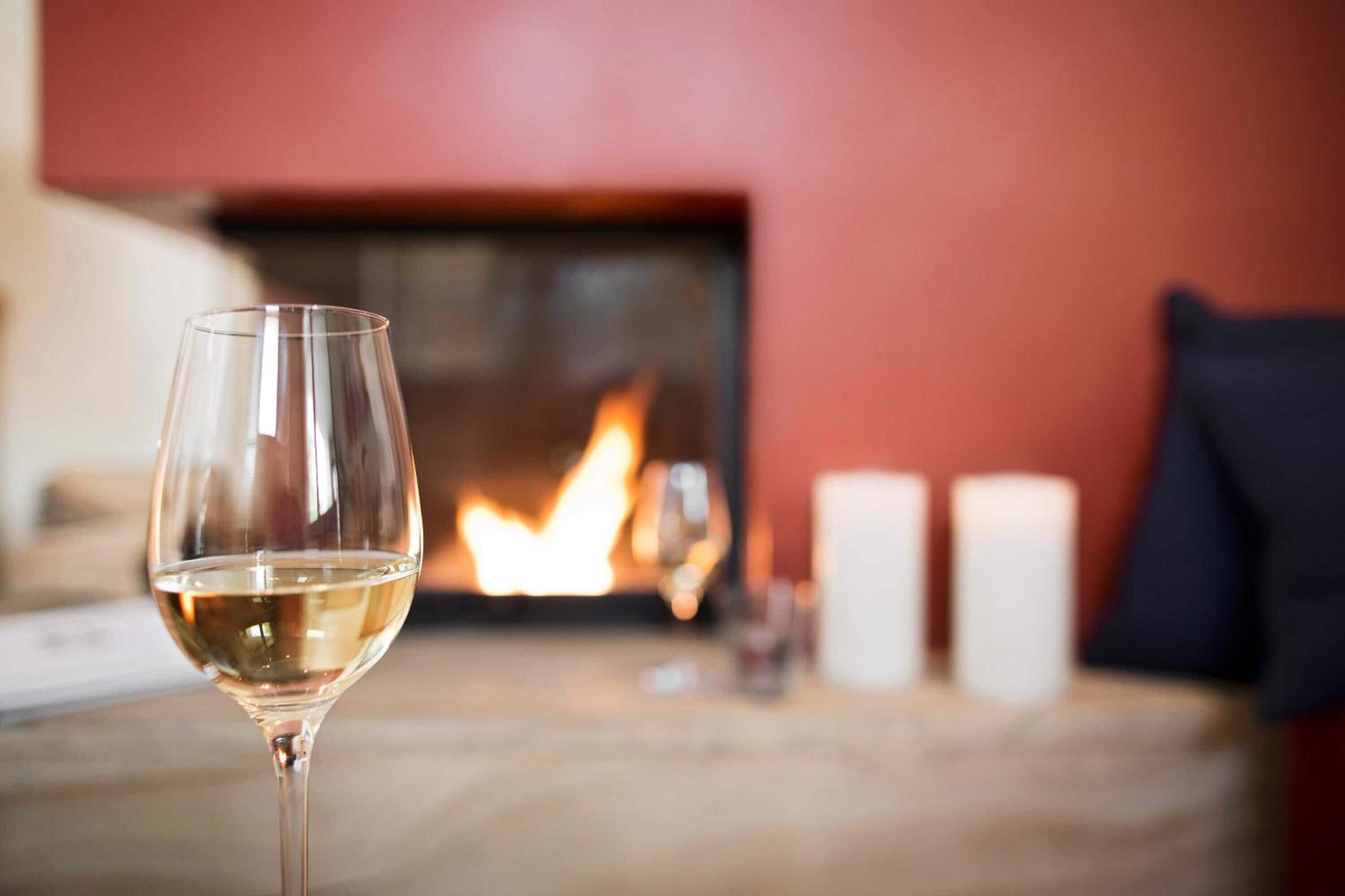 A glass of white wine on a table with a fireplace in the background.