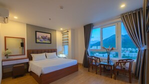 A hotel room with a bed, a desk, a chair, a table, and a large window with curtains. - Canary Nha Trang Hotel (Bac Nha Trang)