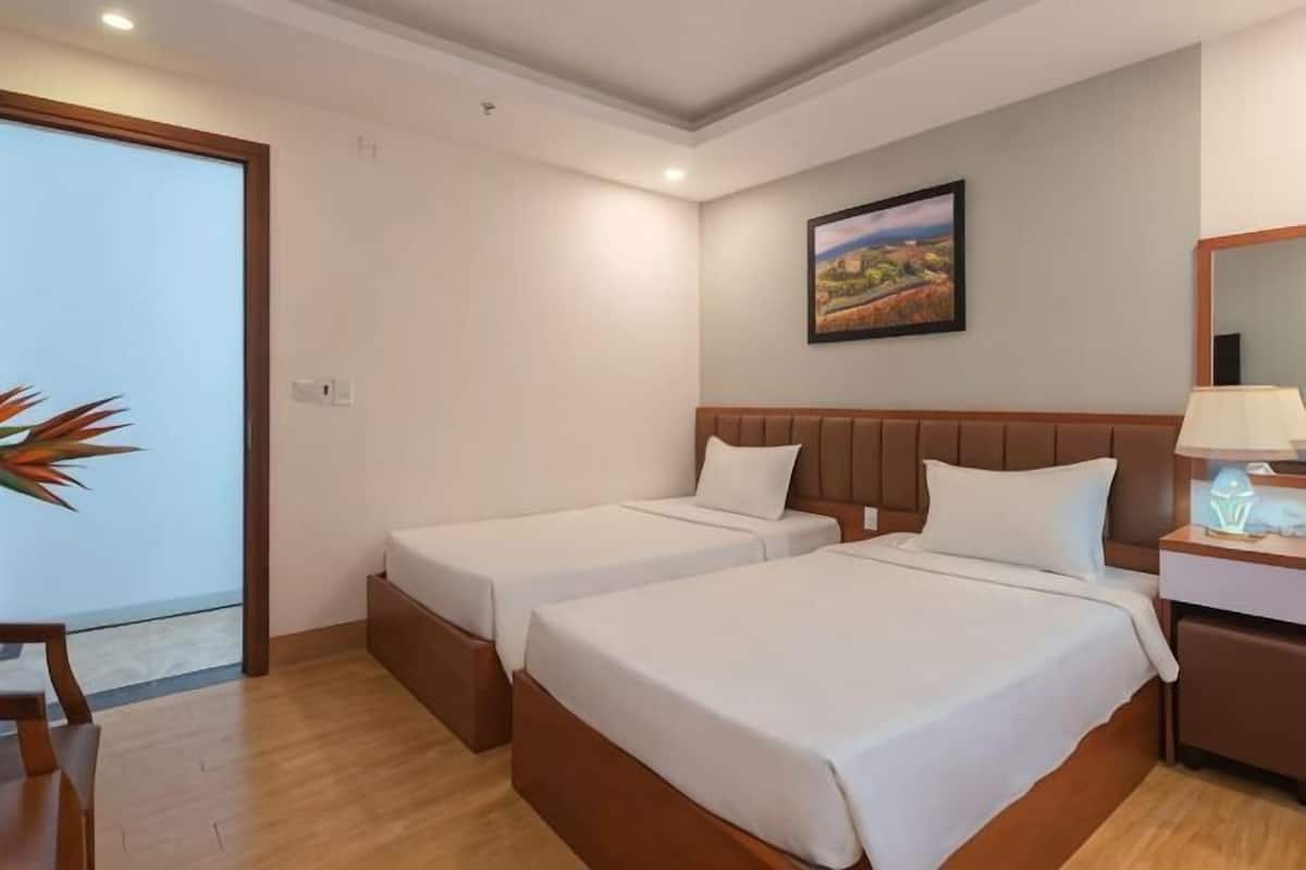 Une chambre d’hôtel avec deux lits, un plancher en bois, un tableau au mur et un bureau avec une lampe.