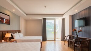 A hotel room with two beds, a TV, a desk with chairs, and a balcony with a mountain view. - Canary Nha Trang Hotel (Bac Nha Trang)