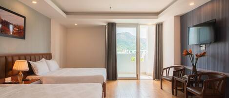 Habitación de hotel con dos camas, televisión, escritorio con sillas y balcón con vista a la montaña.