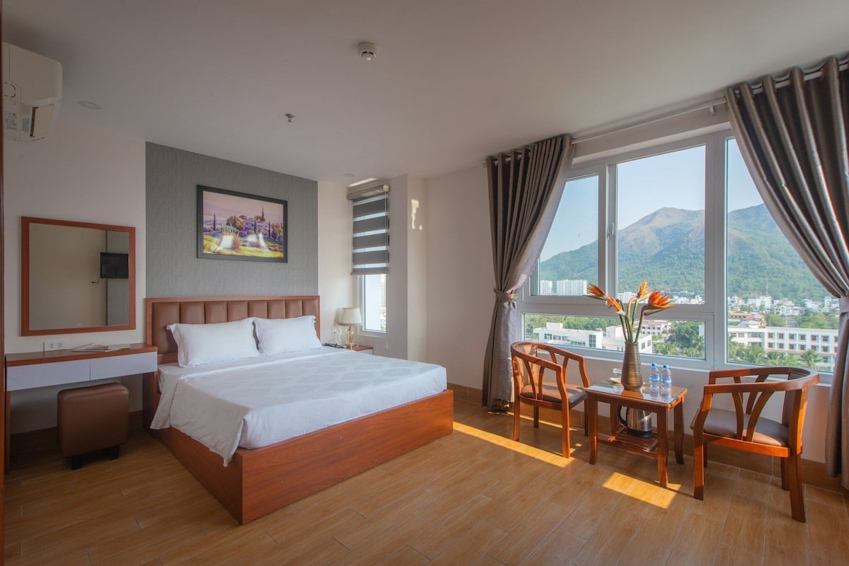 Une chambre d’hôtel avec un grand lit, un bureau avec deux chaises, une fenêtre donnant sur les montagnes et un tableau au mur.