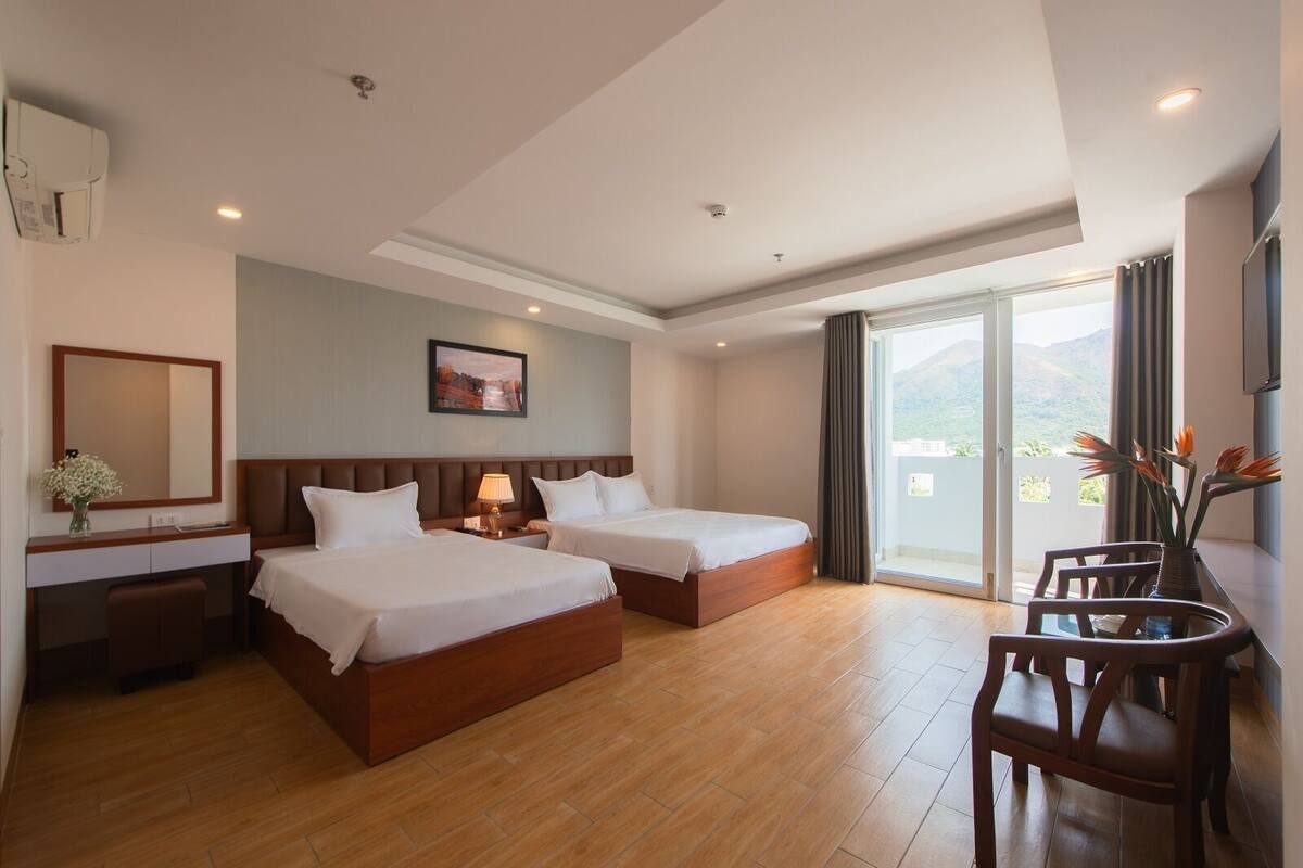 Une chambre d’hôtel avec deux lits, un bureau avec une chaise, une grande fenêtre donnant sur les montagnes et un tableau accroché au mur.