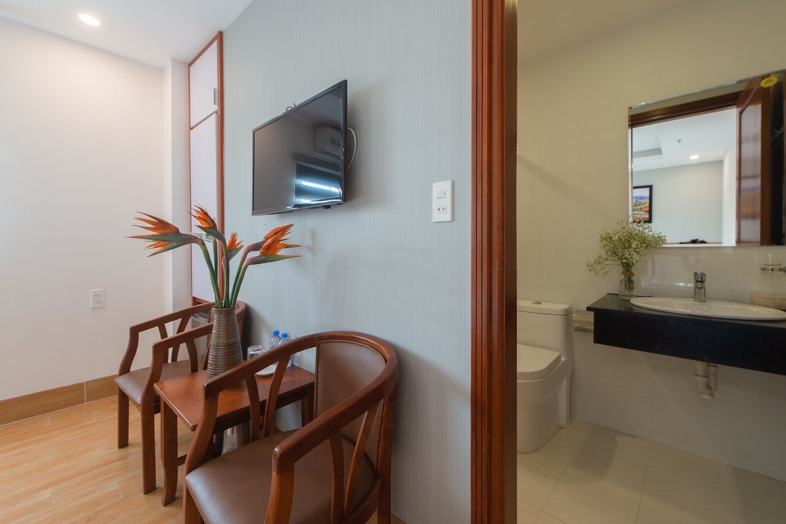 Een hotelkamer met een eethoek, inclusief een houten tafel en stoelen, een vaas met oranje bloemen en een flatscreen televisie aan de wand.
