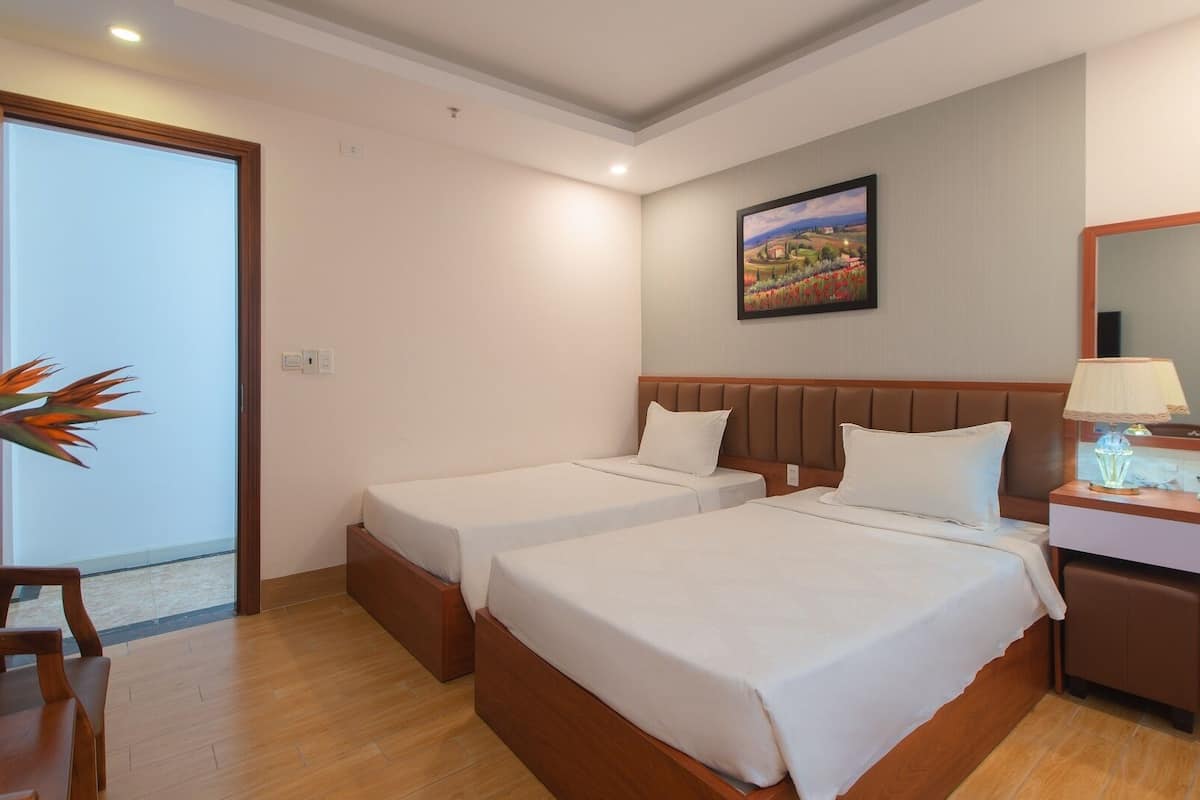 Une chambre d’hôtel avec deux lits, une tête de lit en bois, un bureau avec une lampe et un tableau au mur.