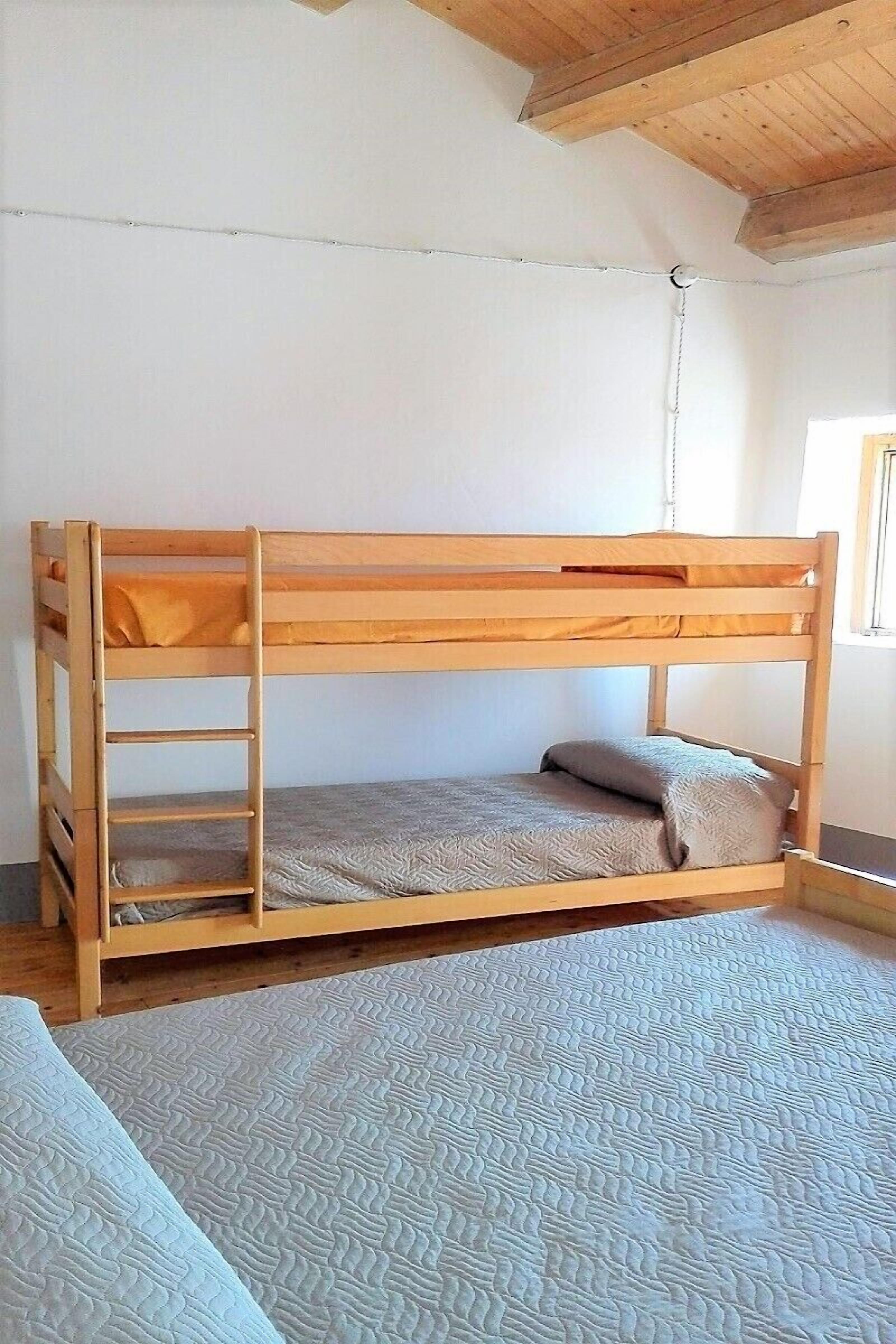 Ein Etagenbett mit einer Treppe, einer grauen Matratze und einem Kopfkissen.