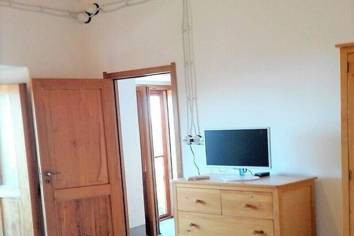 Un dormitorio con una cama, un aparador de madera, un televisor encima y una puerta que da a otra habitación.
