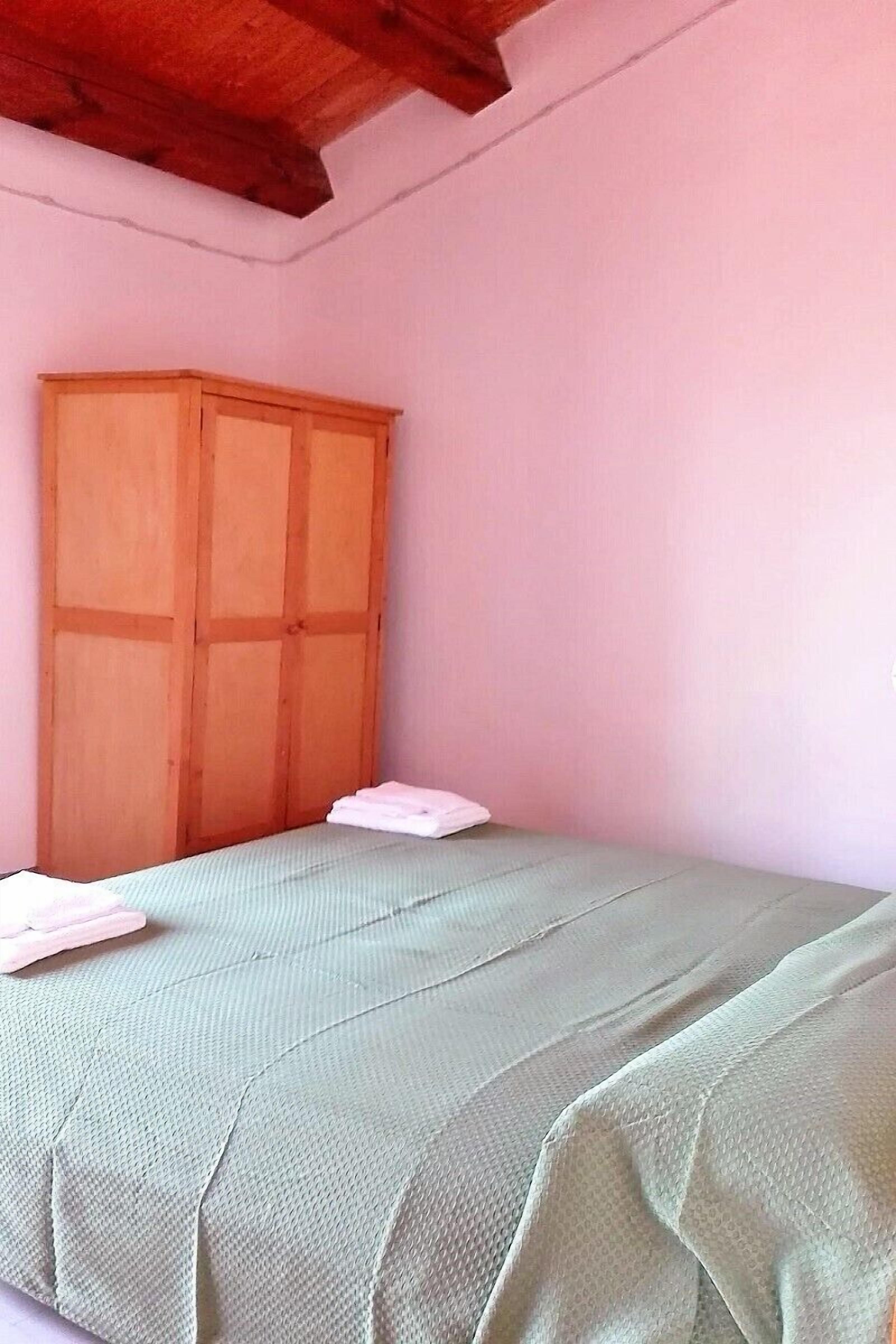 Une chambre avec un lit, une armoire en bois et un mur rose.