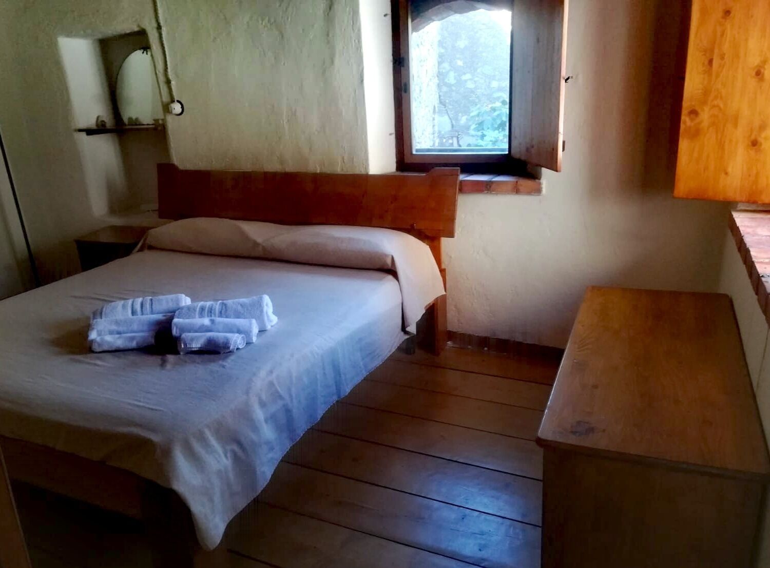 Un lit simple avec une tête de lit en bois, une petite table de chevet et une fenêtre donnant sur les arbres.