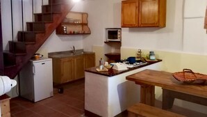 A compact kitchen with wooden cabinets, a small refrigerator, a microwave, and a wooden table with a basket. - Case Rurali Pentedattilo (Melito di Porto Salvo)