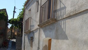 A narrow street with a building featuring a balcony and a stone wall. - Case Rurali Pentedattilo (Melito di Porto Salvo)