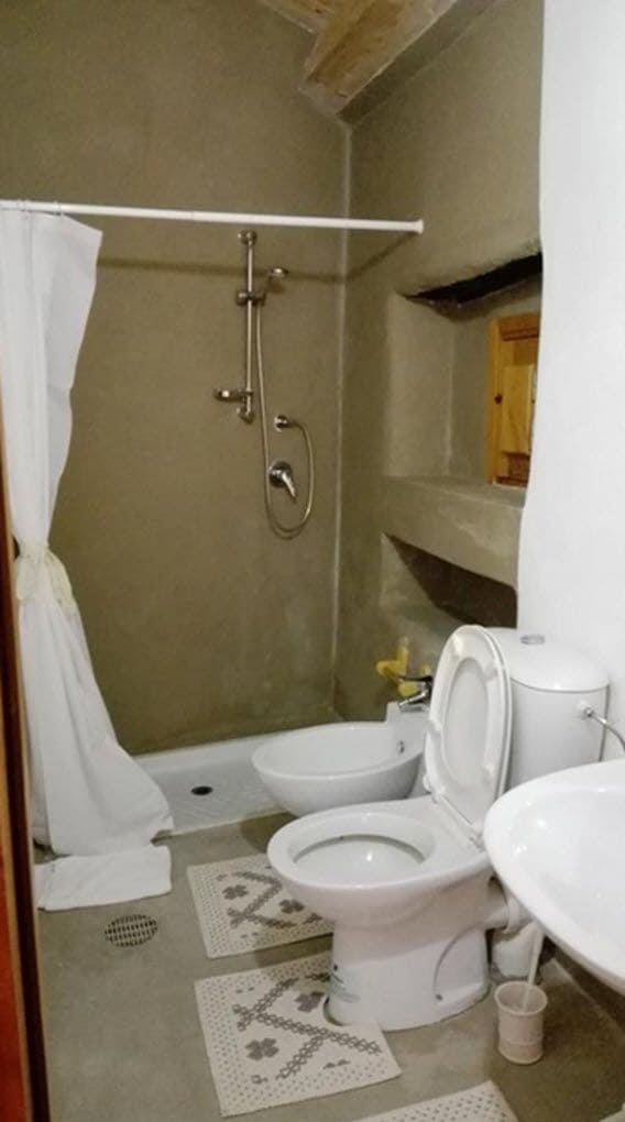 Un baño pequeño con ducha, dos inodoros y un lavabo.