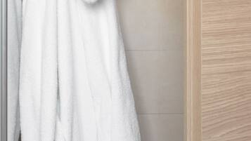 Un peignoir blanc est accroché à un crochet dans une salle de bain dont la porte est en bois et les murs sont recouverts de carreaux.